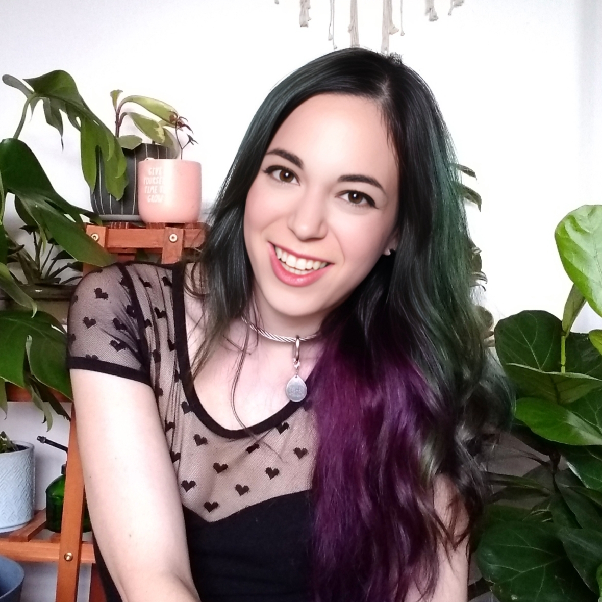 Headshot of Allison Darcy Mitteer. She is positioned in front of several large houseplants.