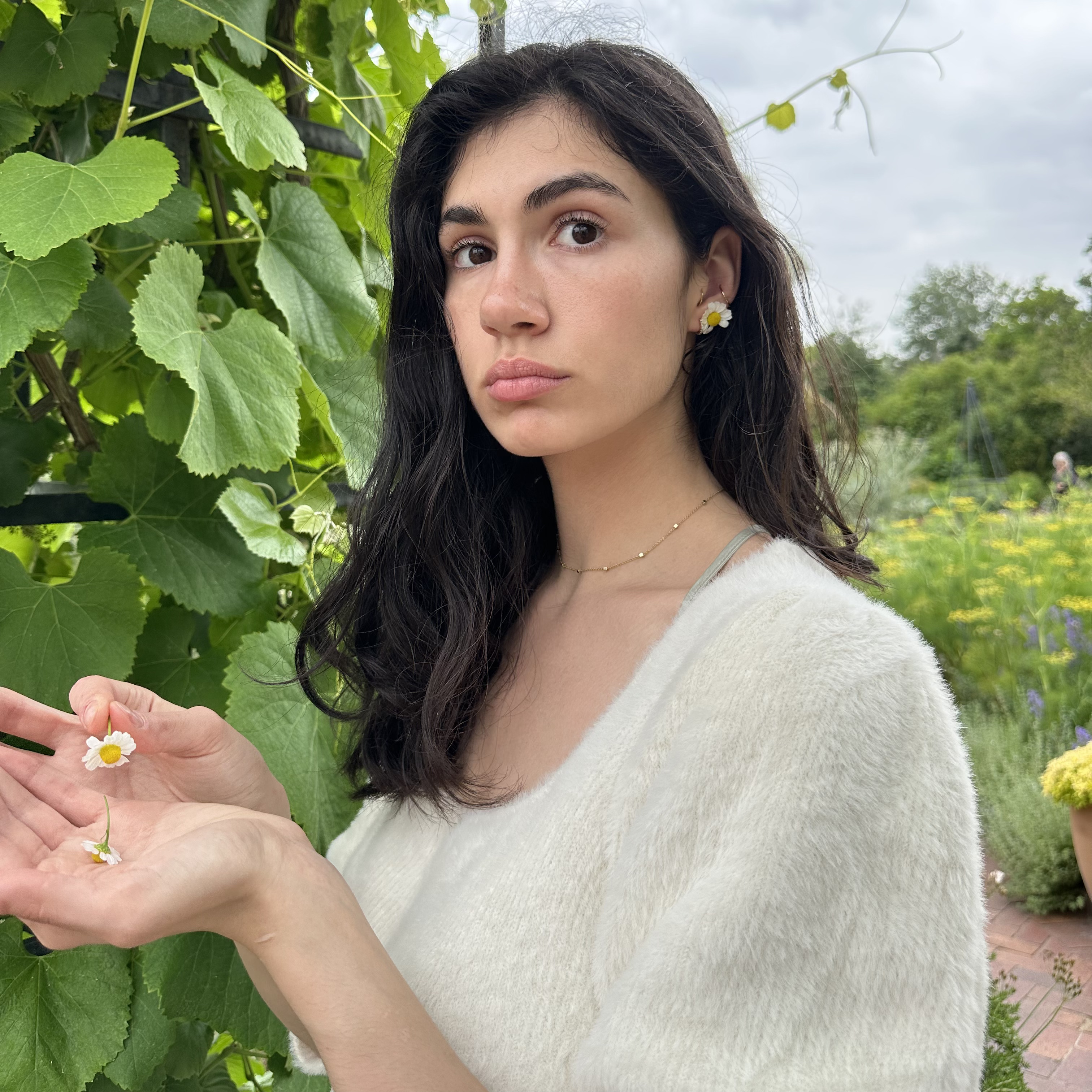 Headshot of Sai. She is standing in a field of plants and holding a small flower in her hands.